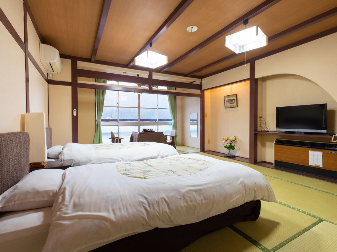 Quarto de hotel com duas camas, televisão, escrivaninha e vista para o mar.