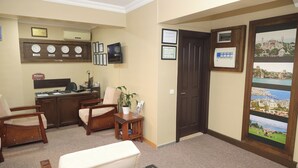 Zona de recepción con un mostrador, sillas, una planta, certificados enmarcados y una puerta con vista a la ciudad.