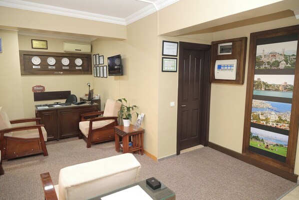 A reception area with a desk, chairs, a plant, framed certificates, and a door with a view of a cityscape.