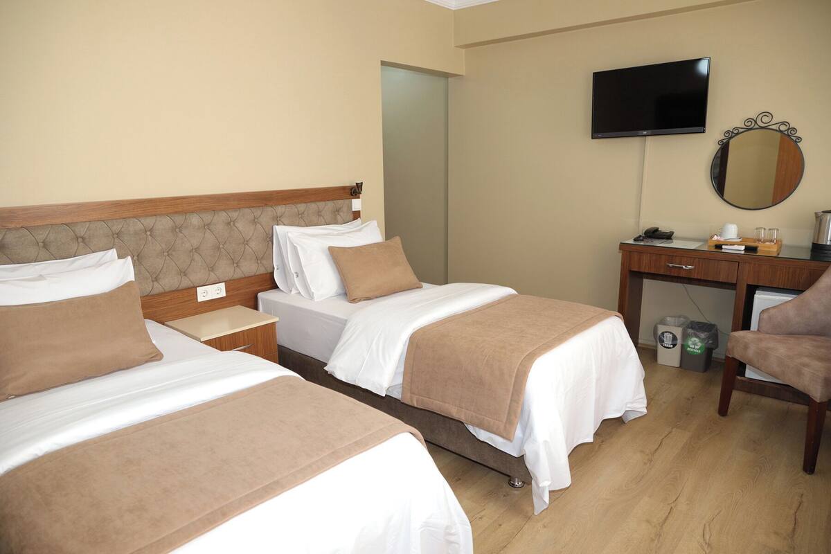 A hotel room with two beds, a desk, a chair, a TV, and a mirror.