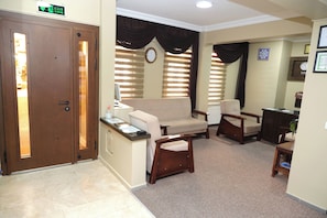 Un área de recepción con una puerta de madera, un sofá, dos sillones, una mesita y un reloj en la pared.