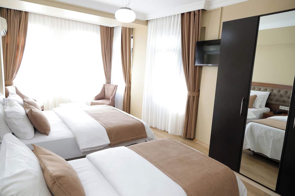 A hotel room with two beds, a chair, a TV, and a wardrobe.