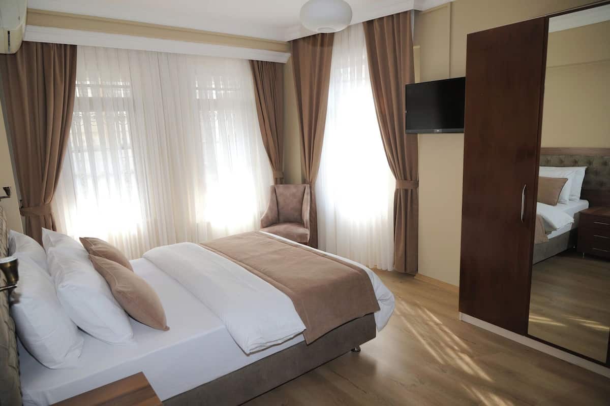 A hotel room with a large bed, a chair, a TV, and a wardrobe.