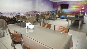 Un comedor con mesas y sillas, un gran mural en la pared y un televisor colgado sobre las mesas.