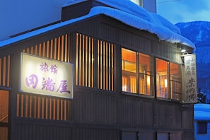 Un edifici amb un cartell en japonès, façana de fusta i neu a la teulada.