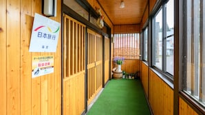 A corridor with wooden walls, a green carpet, and a window with a view of the street. - Iyashinoyado Ryokan Tabataya (Myoko)