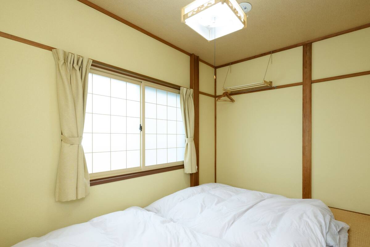 A bedroom with a bed, a window with curtains, and a ceiling light fixture.