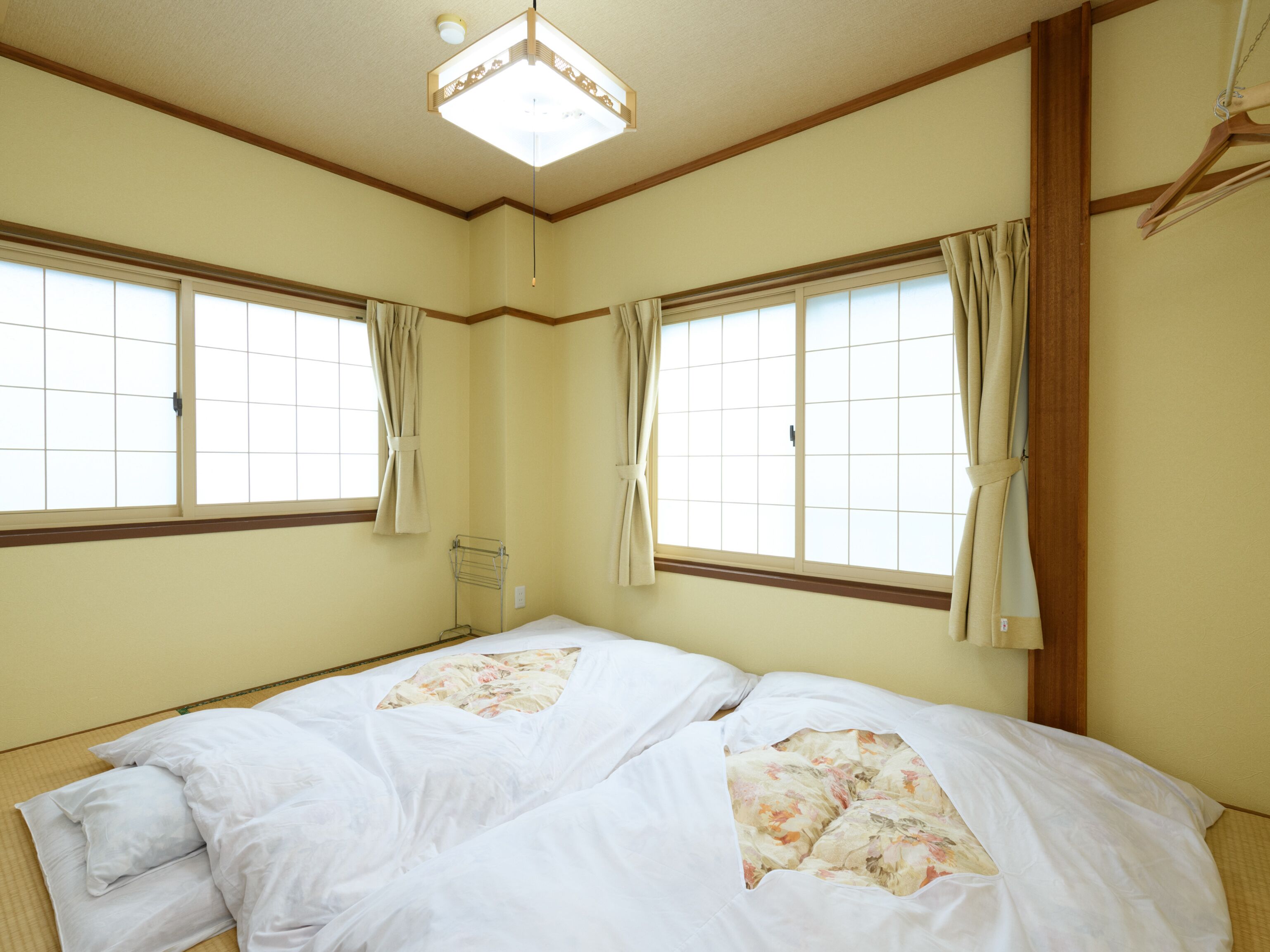 Quarto com duas camas, luminária no teto e janelas com cortinas.