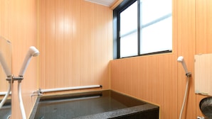 A bathroom with a wooden wall, a window, a bathtub, and a shower area. - Iyashinoyado Ryokan Tabataya (Myoko)