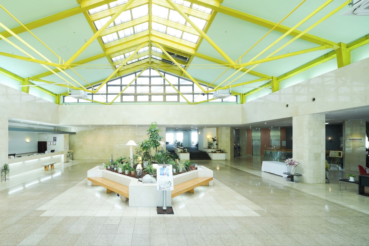 A spacious lobby with a high ceiling, a reception desk, and a central planter with various plants.