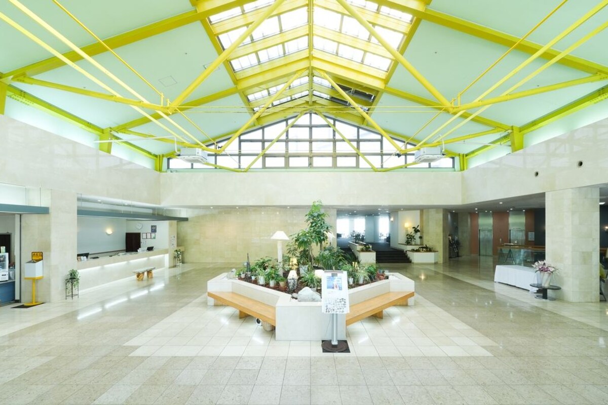 A spacious lobby with a high ceiling, a reception desk, seating areas, and a central plant arrangement.