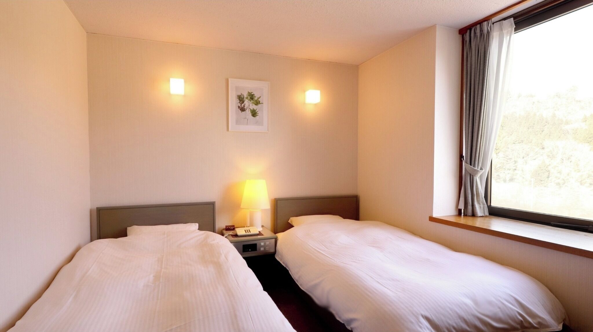 Camera d'albergo con due letti singoli, un comodino con lampada, una sveglia e una finestra con tende.