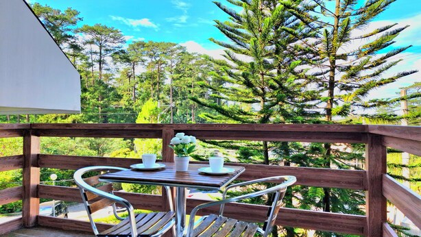 A wooden deck with a table and chairs, overlooking a forested area. - Prestige Vacation Apartments - Hanbi Mansions (Baguio)