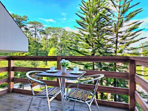 A wooden deck with a table and chairs, overlooking a forested area. - Prestige Vacation Apartments - Hanbi Mansions (Baguio)