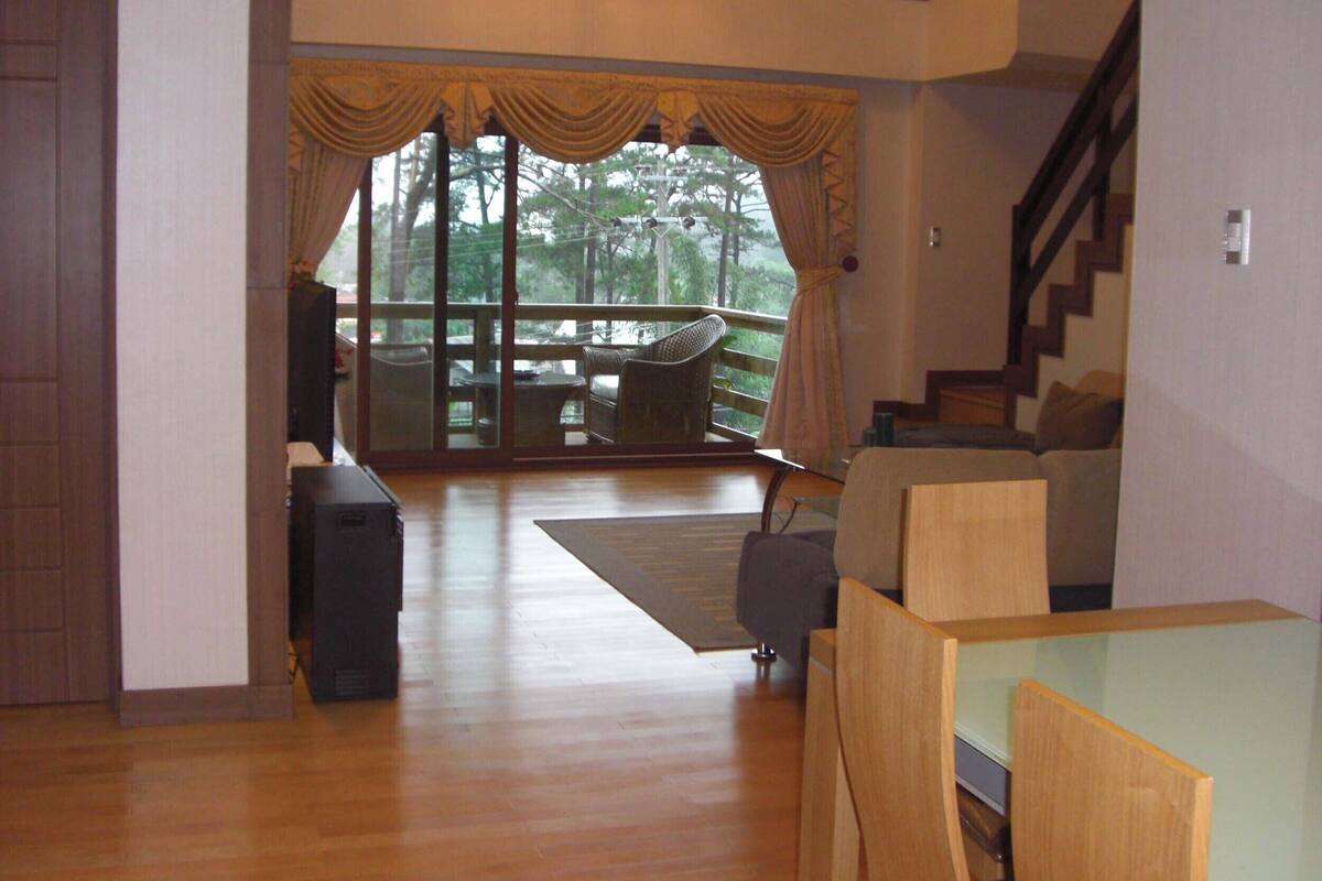 A spacious living area with a wooden floor, a sofa, a coffee table, and a view through large glass doors to an outdoor deck.