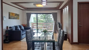A modern living room with a glass dining table, a sofa, and a view of a balcony with a wooden railing. - Prestige Vacation Apartments - Hanbi Mansions (Baguio)