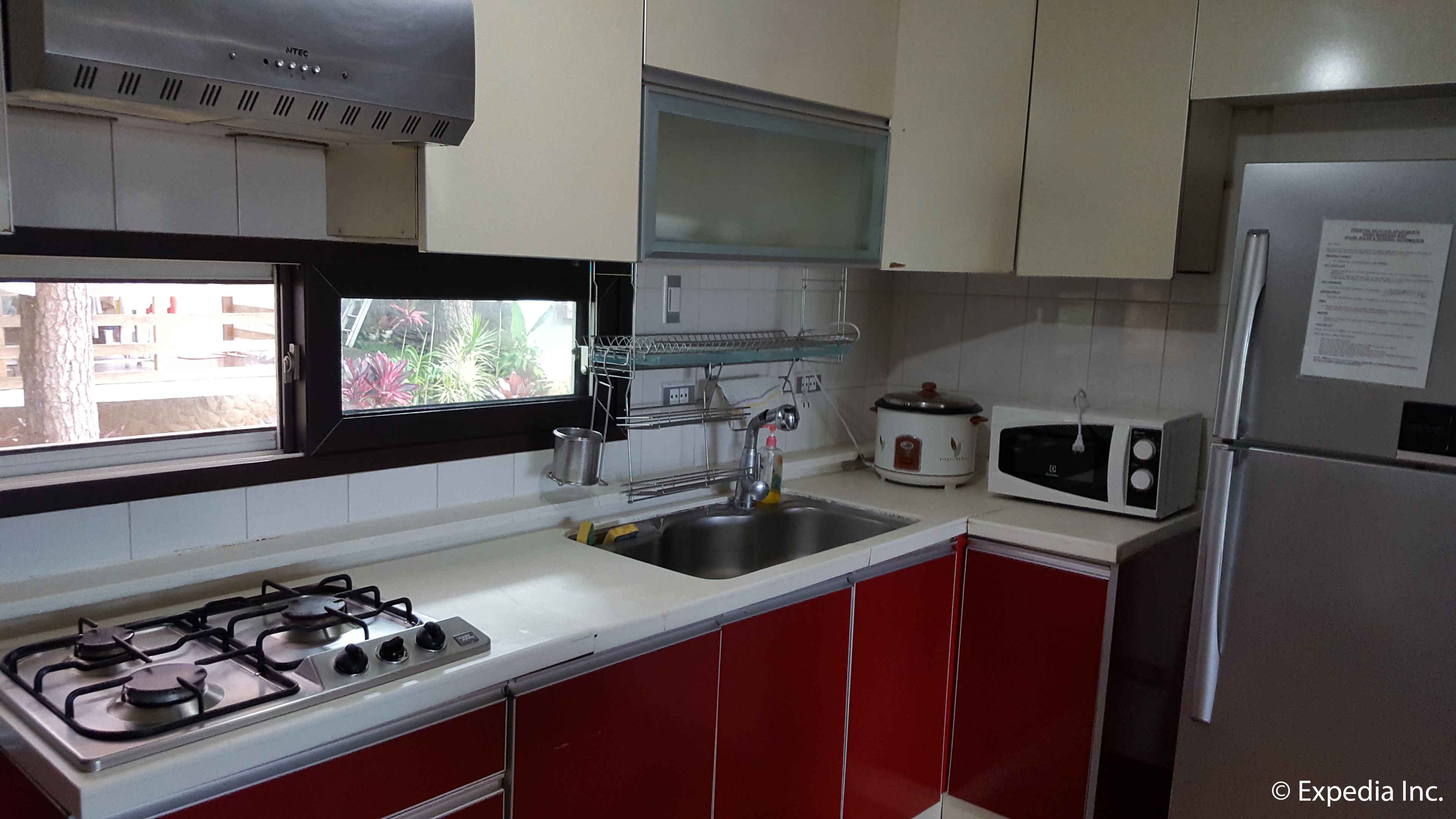 A kitchen with a gas stove, stainless steel sink, white and red cabinets, a microwave, and a refrigerator.