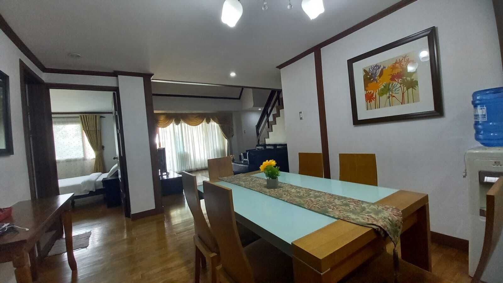A dining area with a long table, chairs, a water dispenser, and a staircase leading to another room.