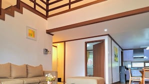 A modern living room with a sofa, ottoman, glass coffee table, and a kitchen visible through an open door. - Prestige Vacation Apartments - Hanbi Mansions (Baguio)