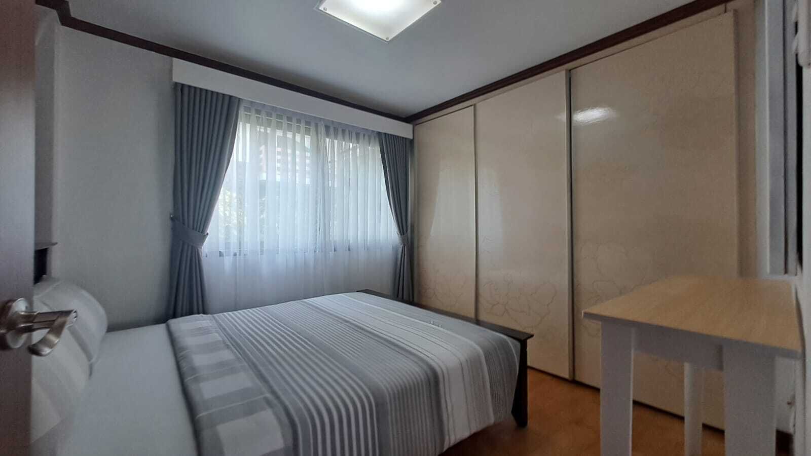 A bedroom with a bed, a bedside table, a wardrobe, and a window with curtains.