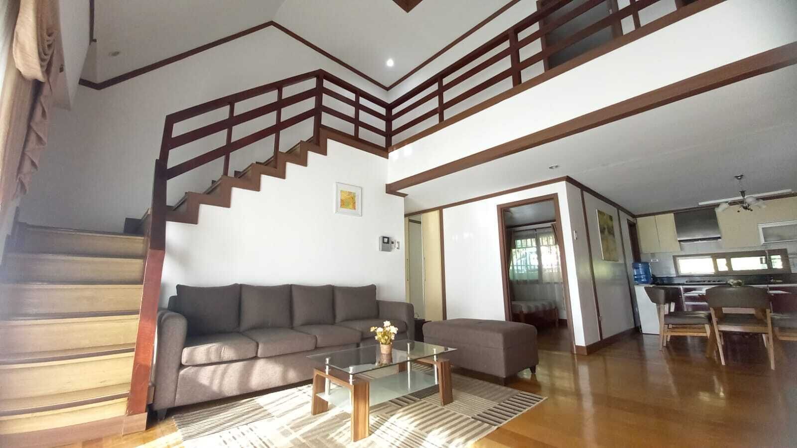 Un vaste espace de vie comprenant un escalier, un canapé, une table basse et une cuisine en arrière-plan.
