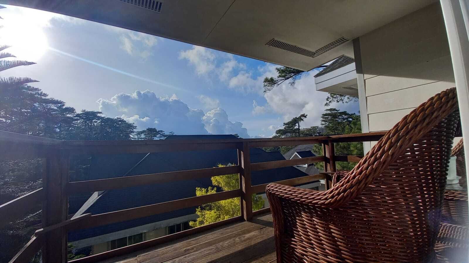 Un balcon avec un fauteuil en osier, une balustrade en bois et une vue sur le ciel et les nuages.
