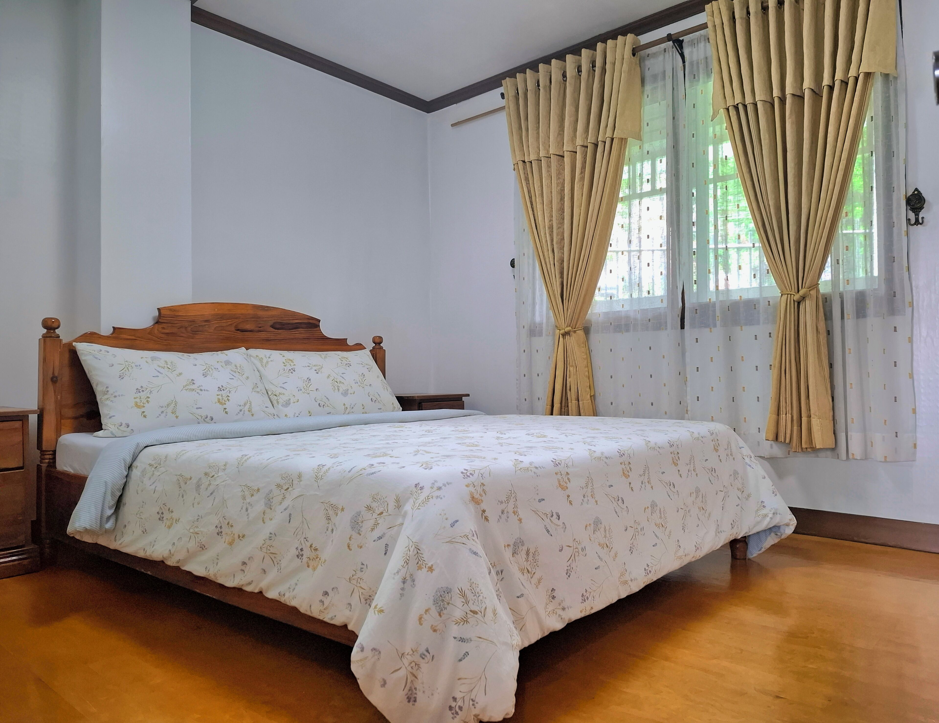 A neatly made bed with floral bedding, a wooden headboard, and a nightstand beside it.