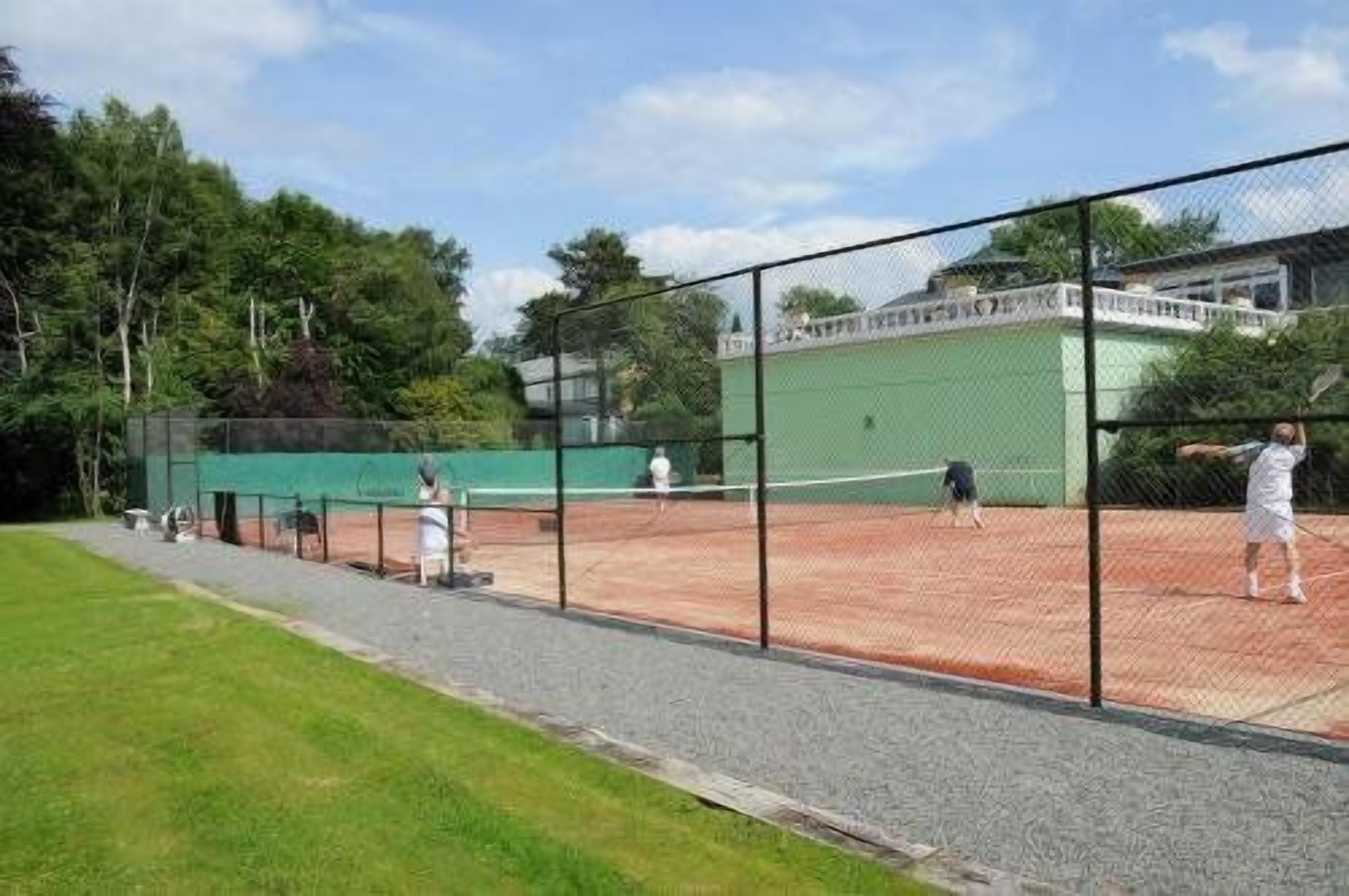 Una cancha de tenis con red, rodeada por una cerca y árboles.