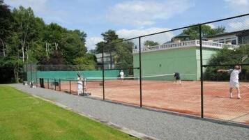 A tennis court with a net, surrounded by a fence and trees.