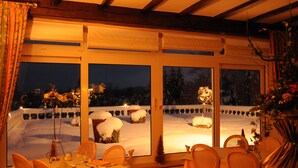 A dining area with a table set for four, large windows with snow-covered outdoor scenery, and a warm interior lighting.