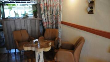 A room with a wooden floor, two brown armchairs, a small wooden table, and a curtain with a floral pattern.