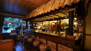 A bar area with wooden stools, a counter with various bottles, and a view of the outdoors through large windows.