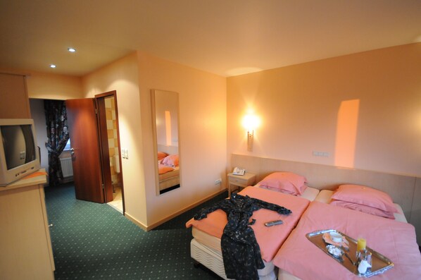 A hotel room with two beds, a TV, a mirror, a bedside table, and a wall-mounted light. - Hotel Hotleu (Waimes)