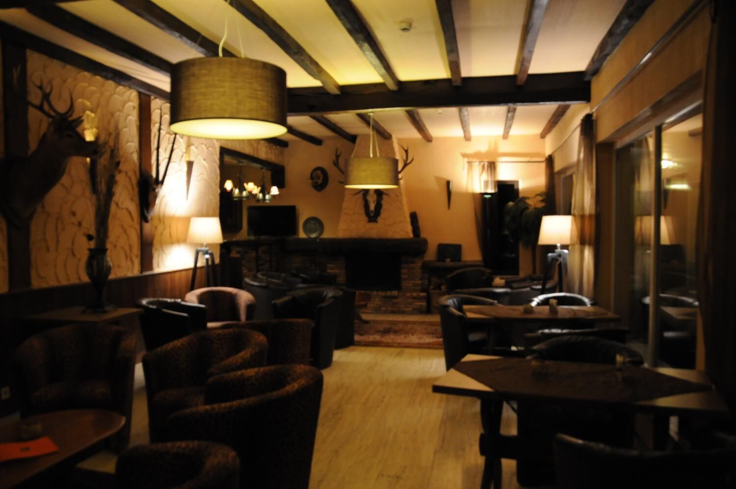 A cozy restaurant interior with wooden beams, plush seating, and a fireplace.