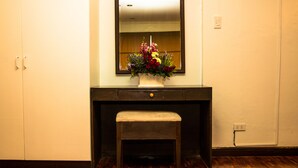 Una habitación con un banco de madera, un escritorio de color oscuro con un cajón y un espejo sobre el escritorio.