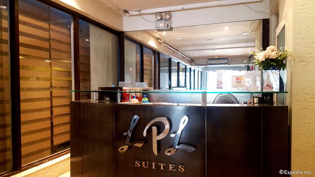 Un mostrador de recepción con detalles en madera oscura, una superficie de vidrio y un logotipo que dice “L P SUITES”. Se observan señalizaciones para Visa y Mastercard, un dispensador de agua y una pequeña planta a la derecha.