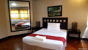 Una habitación de hotel con una cama grande, un cabecero de paneles cuadrados, una mesita de noche con una lámpara y un cuadro en la pared.