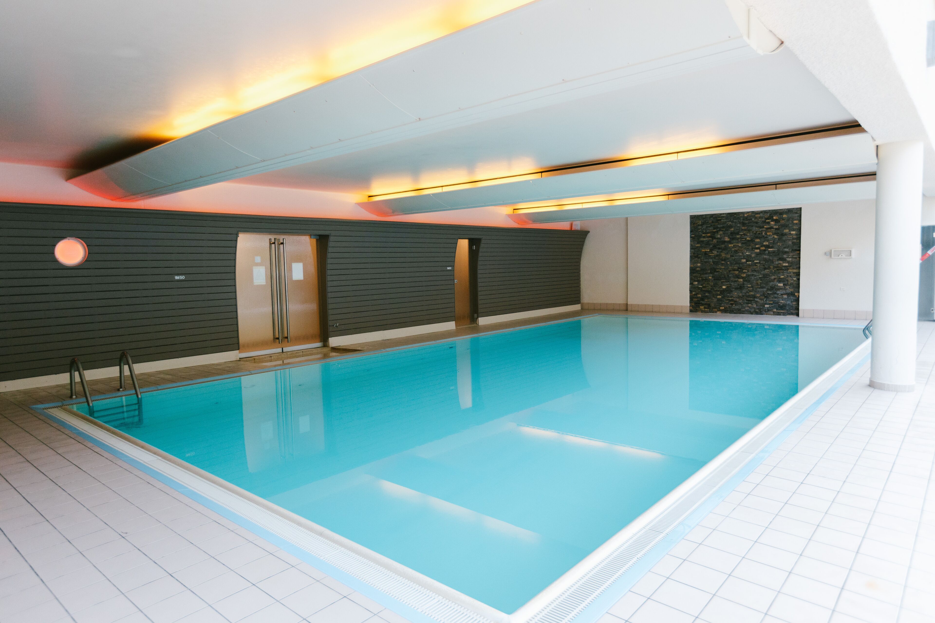 An indoor swimming pool with clear water, tiled walls, and a modern design.