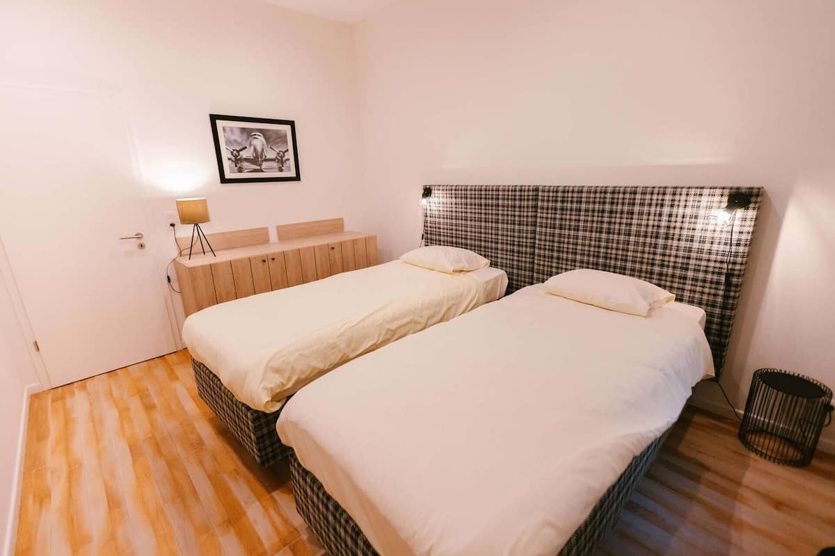 Una habitación con dos camas, cabeceros, mesitas de noche, una lámpara y un cuadro enmarcado en la pared.