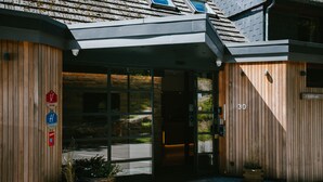 Entrada de hotel con fachada de madera, puertas de cristal y mostrador de recepción.