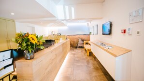 Un área de recepción con un mostrador de madera, un jarrón con girasoles, un sendero que conduce a una zona de estar y un televisor montado en la pared.
