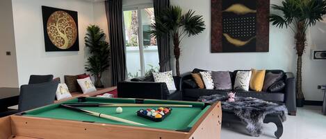 A modern living room with a pool table, a sofa set, and decorative plants.