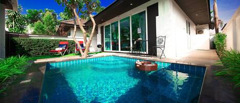 A modern house with a swimming pool, a covered patio, and a large window overlooking the pool.