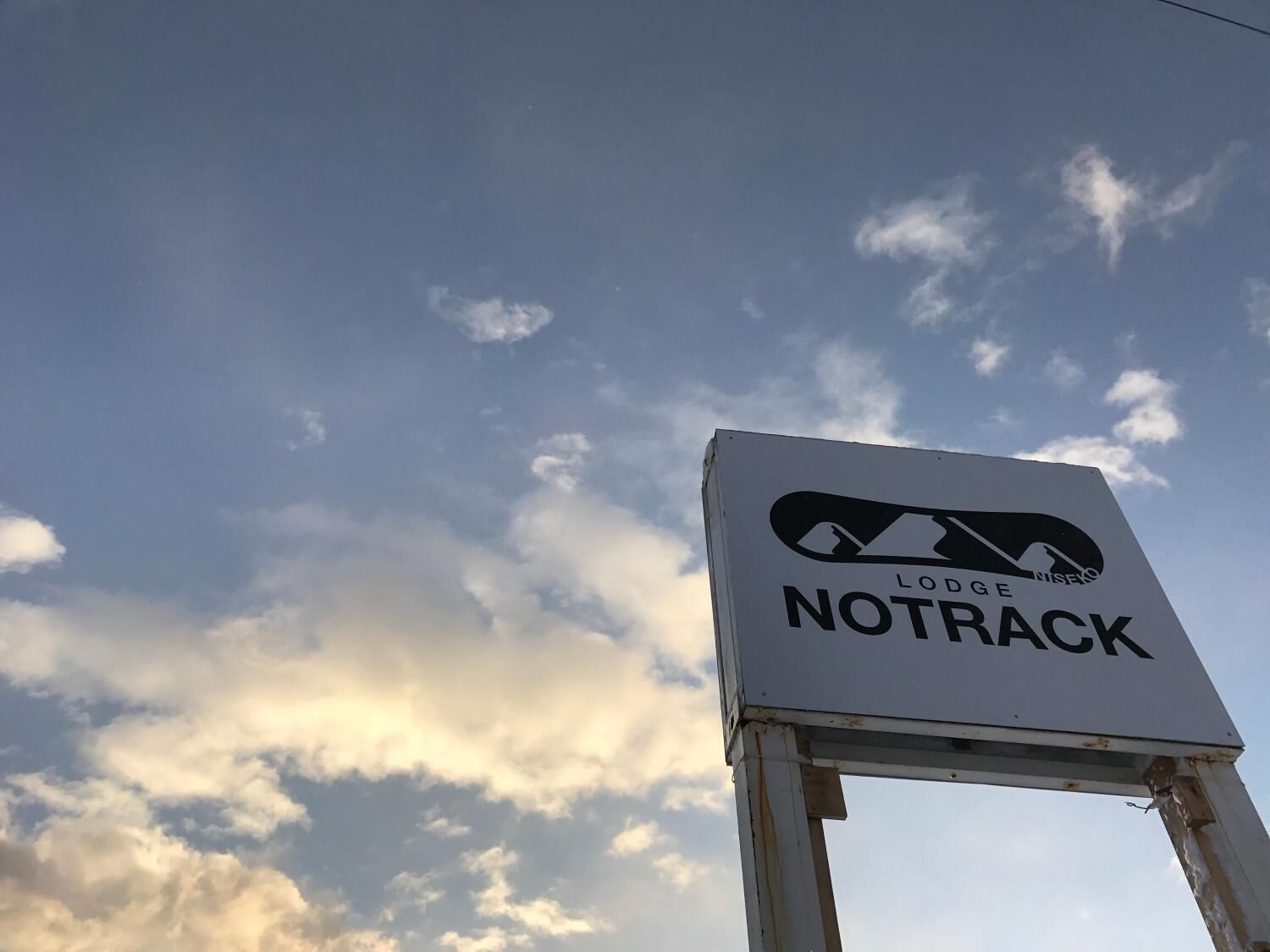 A sign for Lodge Notrack against a sky with clouds.