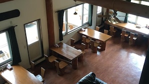 Une salle à manger spacieuse avec de hauts plafonds et des poutres en bois, comprenant plusieurs tables et chaises.