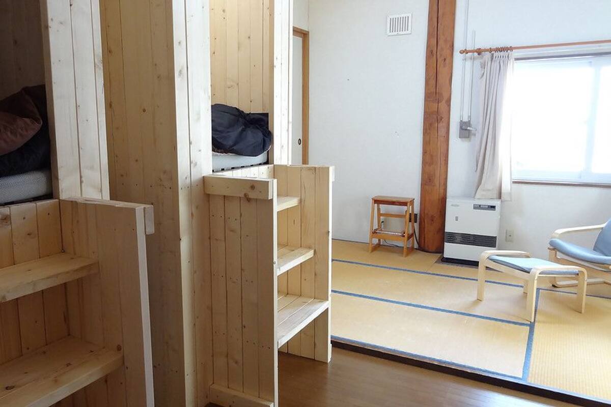 A room with a bunk bed, a small table, a chair, and a window with curtains.