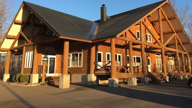 Un grand chalet en bois, doté d’une cheminée imposante, de nombreuses fenêtres et d’un espace d’entrée abrité.