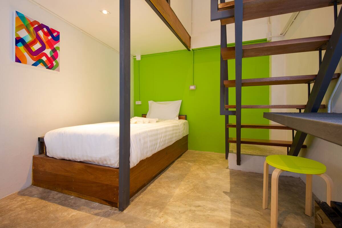 A bedroom with a bed, a green wall, a wooden desk, and a colorful abstract painting.