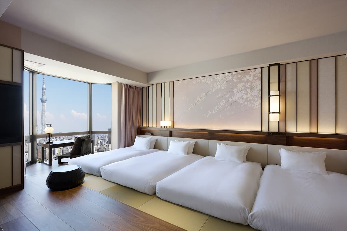 A hotel room with a large bed, a TV, a desk, and a view of a cityscape.