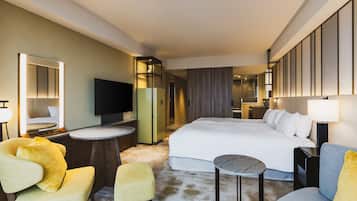 A hotel room with a bed, a TV, a mirror, a small round table, and two armchairs.